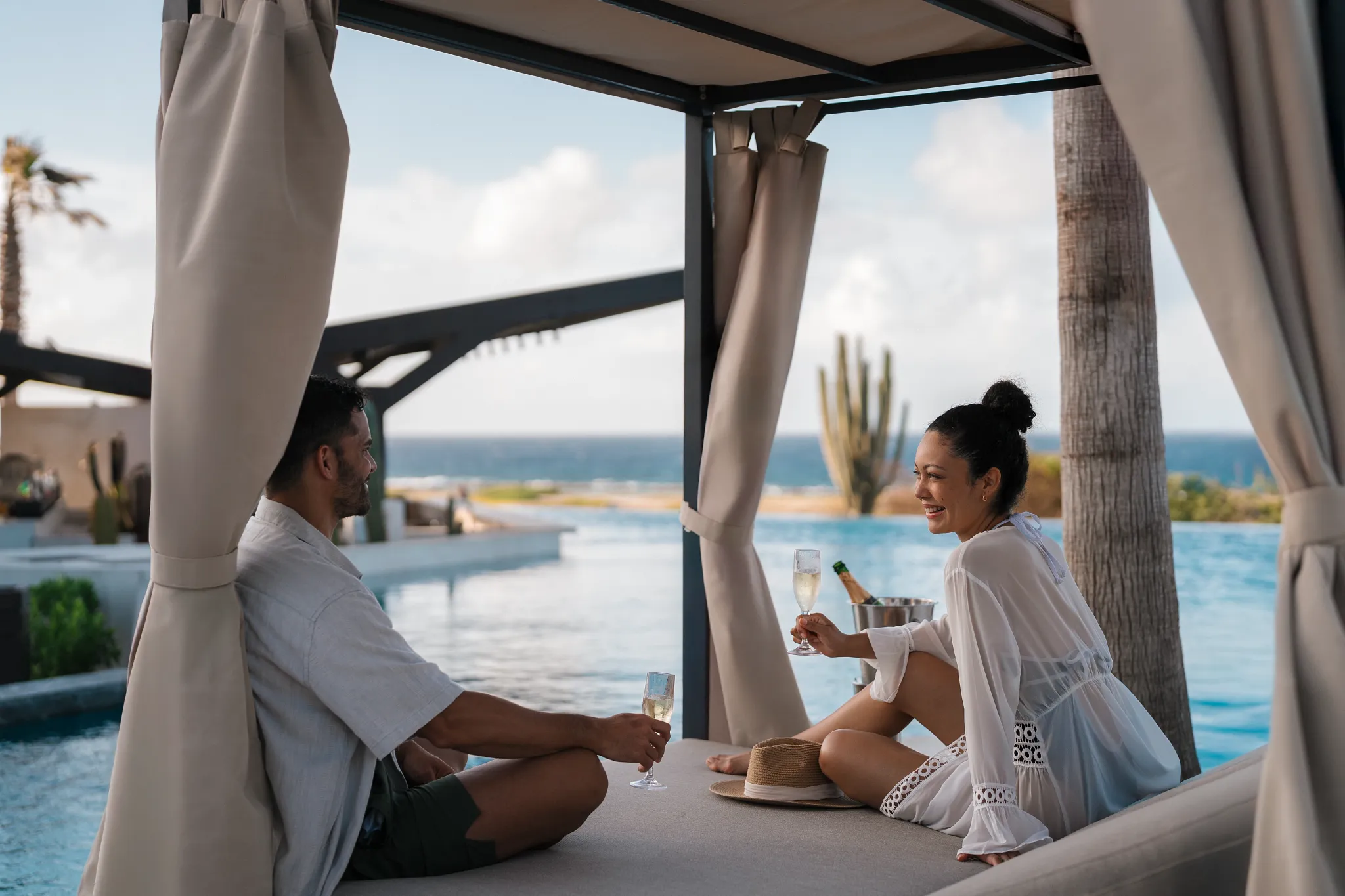 Couple relaxing in a private Bali bed cabana with ocean views at Secrets Baby Beach Aruba.