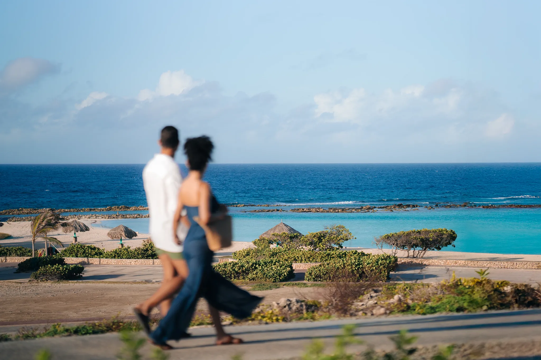 Couple strolling along the scenic coastline near Secrets Baby Beach Aruba with turquoise Caribbean waters in the background.