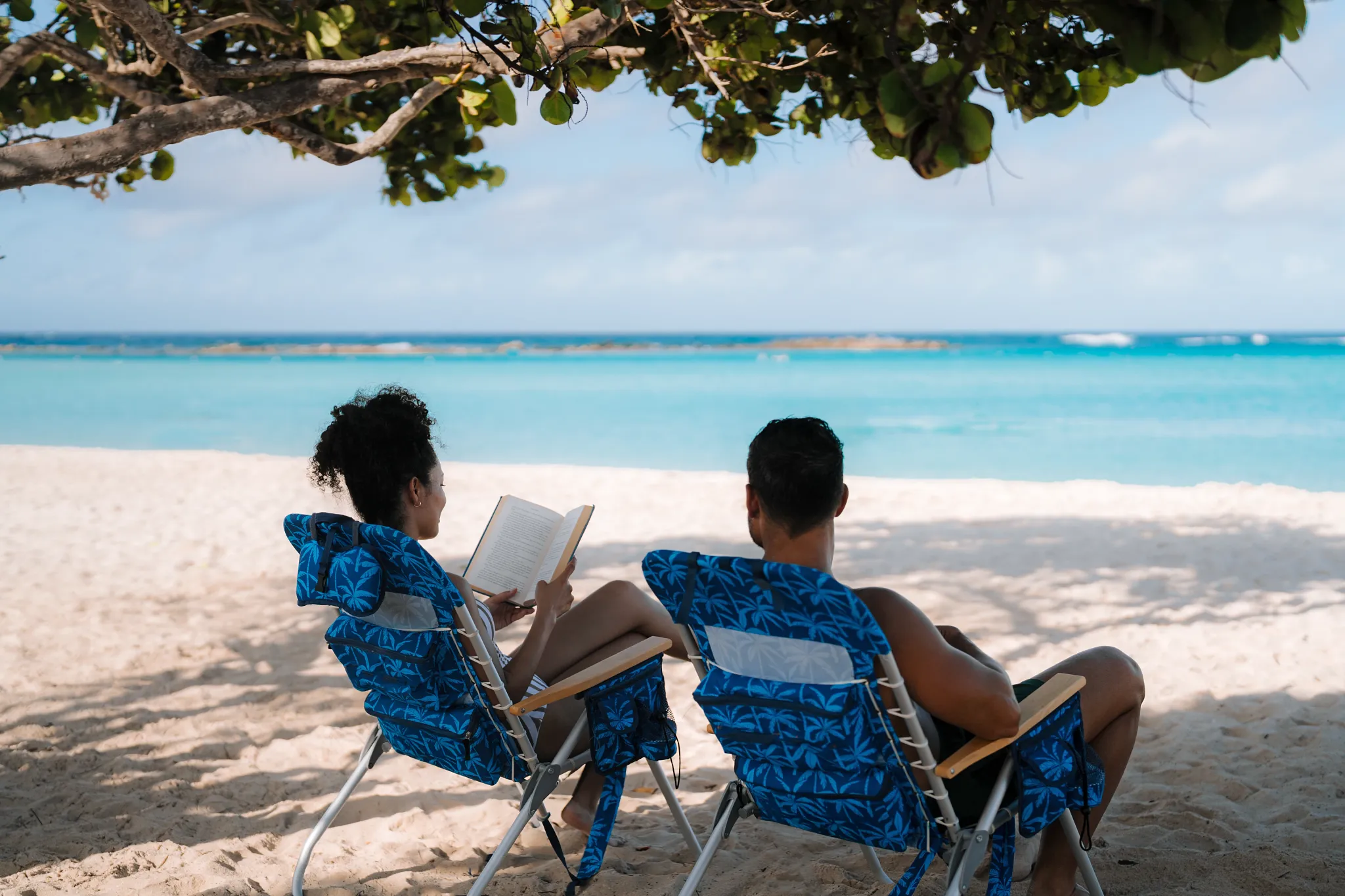 Couple relaxing in beach chairs under tropical shade at Baby Beach near Secrets Baby Beach Aruba.