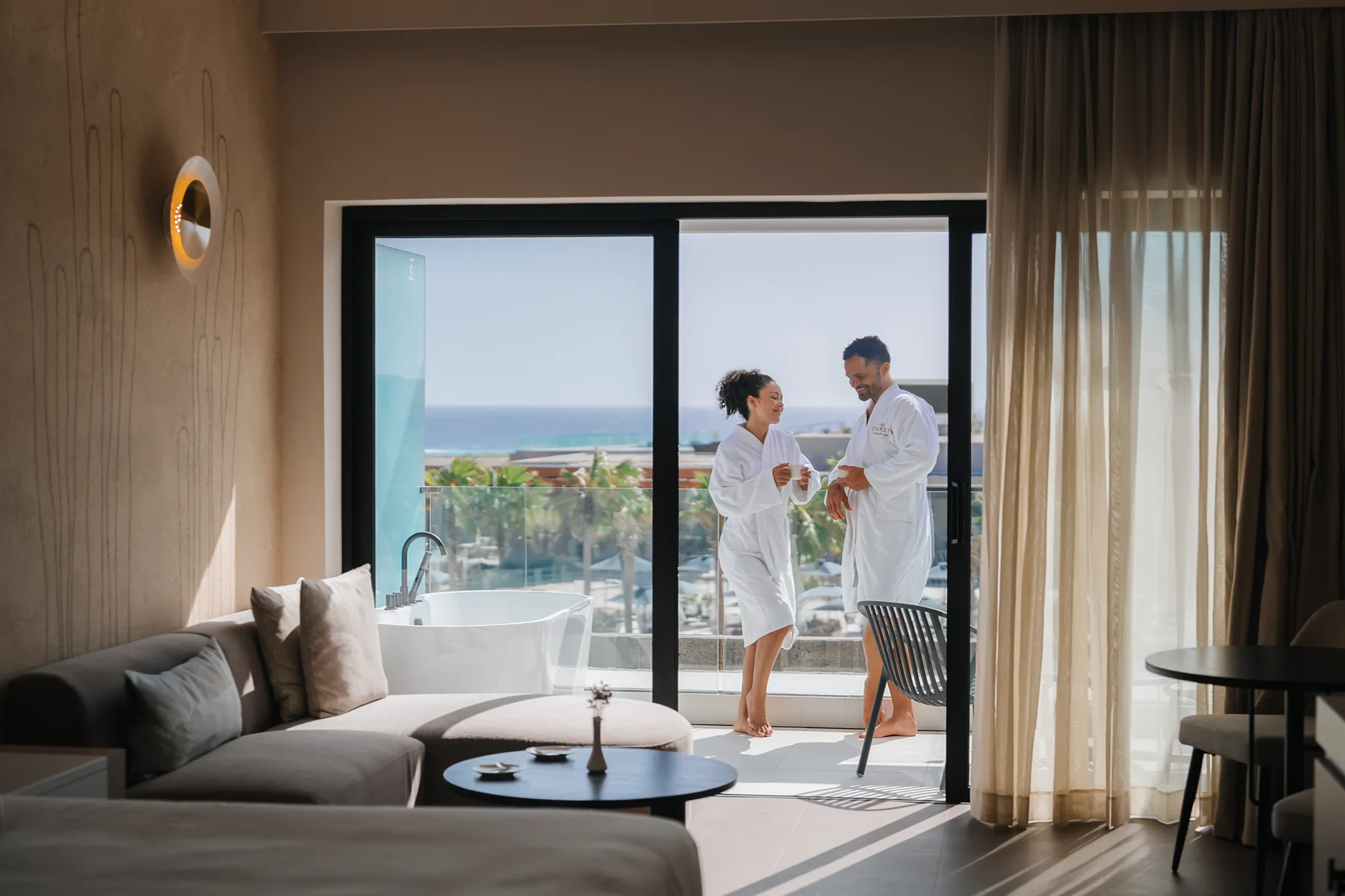 Couple in plush robes enjoying coffee on a private ocean-view balcony at Secrets Baby Beach Aruba.