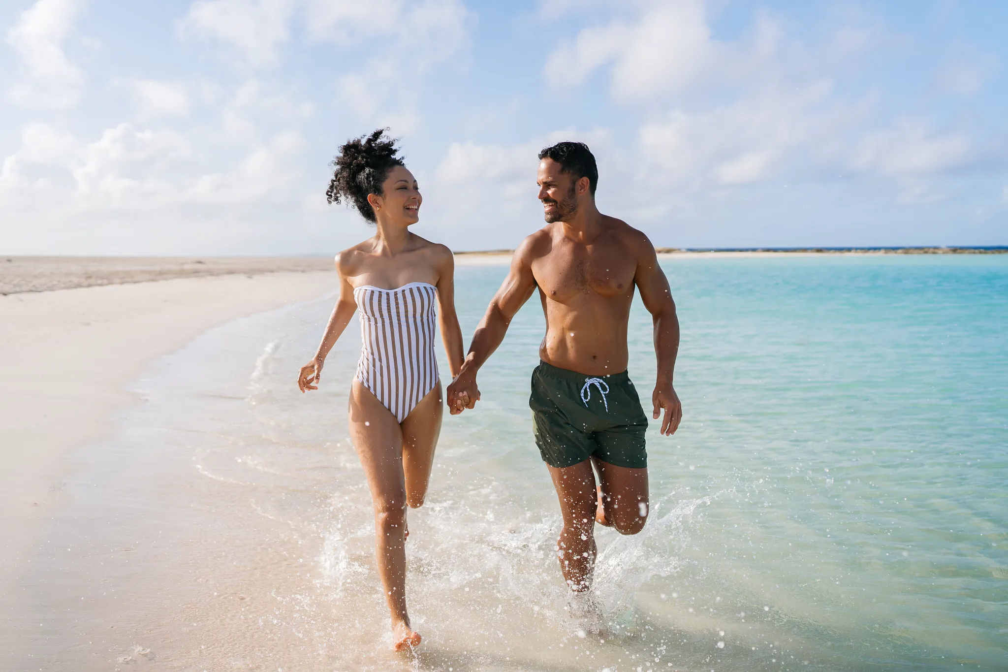 Romantic couple walking hand in hand through shallow turquoise waters at Baby Beach near Secrets Baby Beach Aruba.